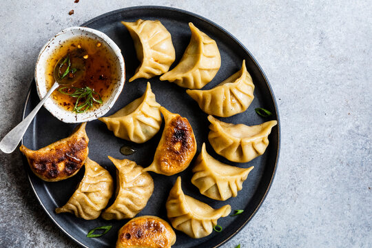 A plate of dumplings with a small bowl of dipping sauce.