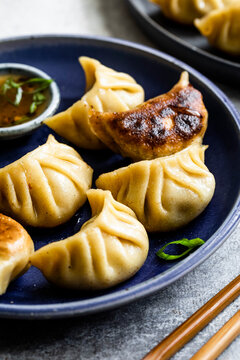 A plate of steamed and pan-fried dumplings served with dipping sauce on a blue plate.