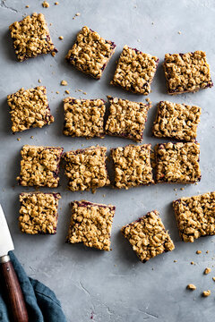 An assortment of oatmeal crumble bars with a berry filling arranged on a gray surface.