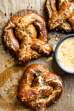 Three salted soft pretzels on parchment paper with a bowl of cheese sauce.