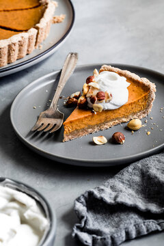 A slice of pumpkin pie topped with whipped cream and nuts on a gray plate with a fork.