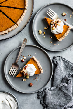 Top view of pumpkin pie slices with whipped cream and nuts on gray plates.