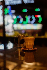 A glass of hot latte with froth art and a jar on the table with bokeh background