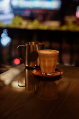 A glass of hot latte with froth art and a jar on the table with bokeh background