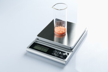 Laboratory scale with beaker of sample on white background