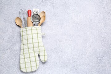 Different kitchen utensils in oven mitten on light table, top view. Space for text