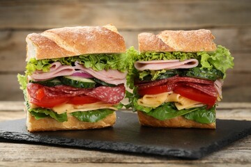 Tasty baguette sandwich with ham and vegetables on wooden table, closeup
