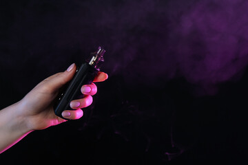 Woman using electronic smoking device in neon lights on black background, closeup. Space for text