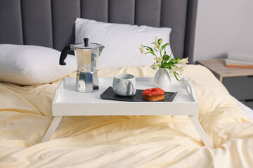 Tray with delicious breakfast and flowers on bed indoors