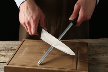 Man sharpening knife with sharpener on wooden table, closeup
