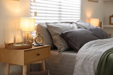 Comfortable bed with soft linens, bedside table and lamp in room. Home textile