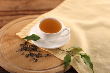 Cup of tasty green tea and leaves on wooden table