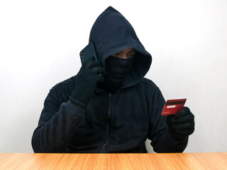 Cyber crime concepts. A male thief holds a smartphone and credit card in his hand and picks up a...