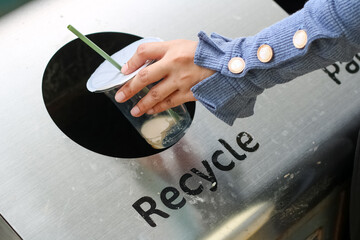 Close up woman hand holding garbage plastic bottle into recycle trash bin, selective focus