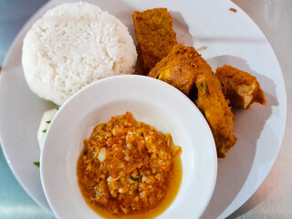Ayam penyet served on a white plate. Indonesian cuisine. With a bowl of spicy sambal