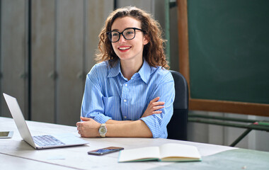 Smiling school professional online teacher coach advertising virtual students classes teaching remote education webinars. Young happy business woman sitting at work desk with laptop. Candid photo