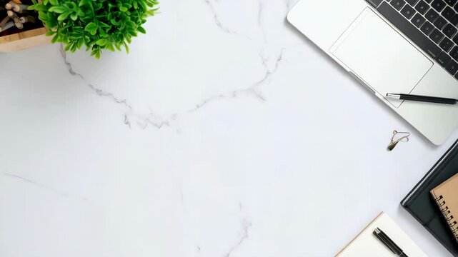 Modern desk setup with laptop, pens, notebooks, pencils, and plant against bright white marble background, overhead composition