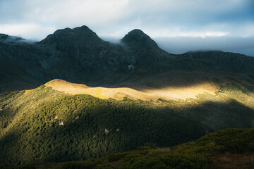 Evening light catching the side of mountains as clouds roll in.