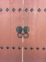 Traditional Korean wooden door with metal decorative studs and ring handles in pink wood.