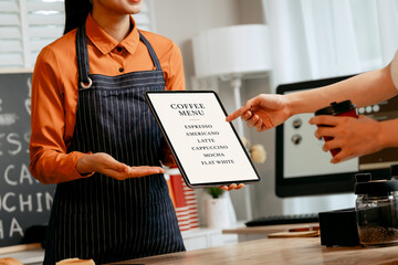 A young Asian female barista in modern cafe assists woman customer ordering latte, fresh coffee beans, dark roast, croissant, completing the purchase with mobile payment at the POS using QR code.