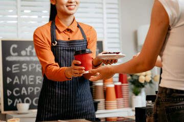 A young Asian female barista in modern cafe assists woman customer ordering latte, fresh coffee...