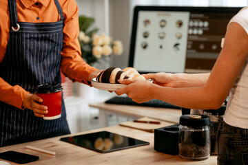 A young Asian female barista in modern cafe assists woman customer ordering latte, fresh coffee beans, dark roast, croissant, completing the purchase with mobile payment at the POS using QR code.