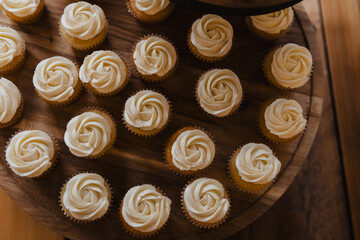 Elegant display of vanilla cupcakes with buttercream rosette frosting on wooden tiered stand — perfect for weddings, parties, dessert menus, and celebration food photography