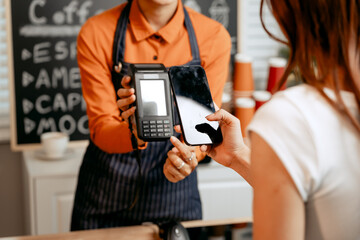 A young Asian female barista in modern cafe assists woman customer ordering latte, fresh coffee beans, dark roast, croissant, completing the purchase with mobile payment at the POS using QR code.