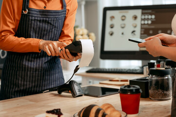 A young Asian female barista in modern cafe assists woman customer ordering latte, fresh coffee...