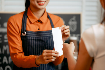 A young Asian female barista in modern cafe assists woman customer ordering latte, fresh coffee beans, dark roast, croissant, completing the purchase with mobile payment at the POS using QR code.