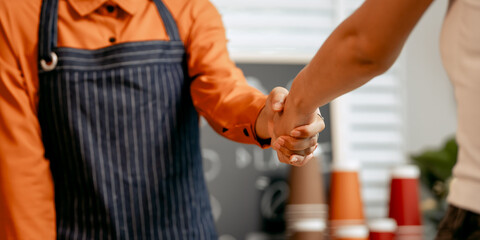 A young Asian female barista in modern cafe assists woman customer ordering latte, fresh coffee beans, dark roast, croissant, completing the purchase with mobile payment at the POS using QR code.