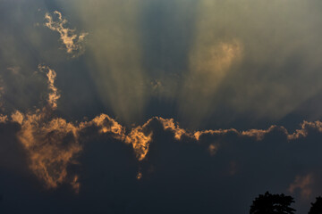 Dramatic sunbeams pierce through dark, orange-lit clouds.