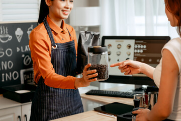A young Asian female barista in modern cafe assists woman customer ordering latte, fresh coffee...