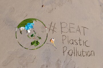 Earth shape with plastic waste texture beside handwritten message “#BEAT Plastic Pollution” on beach sand, representing global awareness of environmental pollution