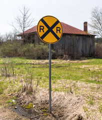 A side of the road railroad crossing sign next to an abandoned building in Columbus, Pennsylvania, USA on a sunny spring day 