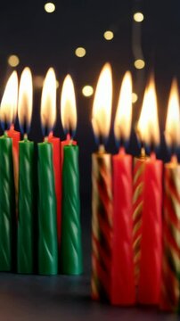 Burning Kwanzaa candles in red, green and gold colors symbolizing the seven principles on black surface with bokeh lights