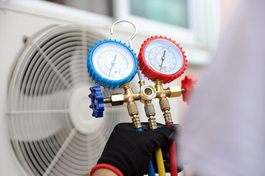 Air conditioning electrical technician using manifold gauge measuring tool checking refrigerant pump filling home air conditioner and maintenance heat fix repair and clean outdoor compressor unit.