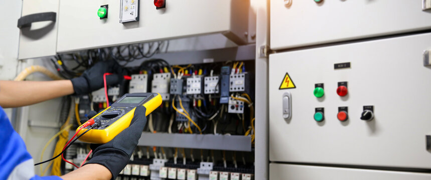 Electrical service technician uses measuring tools equipment checking electricity on circuit breaker panel and check electric cable wiring main power distribution board for maintenance system.