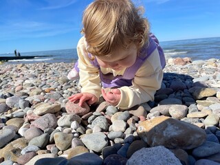 A young child crawls over colorful pebbles at the waters edge The sky is clear and blue creating a warm atmosphere perfect for outdoor play and discovery