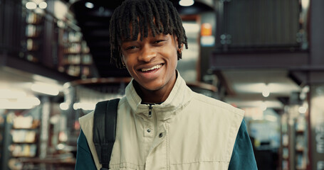 College student, happy and man with backpack in library for night study, research and education. Portrait, learning and black person with smile on campus for essay deadline and assignment information