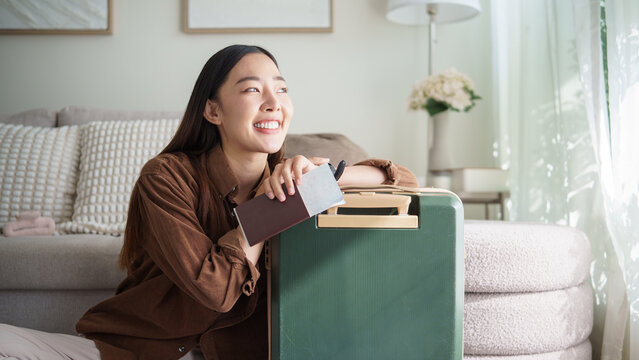Smiling woman sitting with luggage, holding a passport and boarding pass, ready for travel. - Powered by Adobe