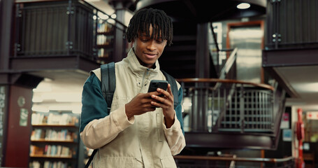 Phone, happy and black man in university library with contact, networking or email for scholarship. Smile, connectivity and African student with cellphone for communication on mobile app at college.