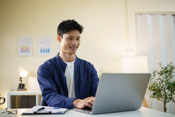 Asian businessman analyzing data on laptop computer in bright workspace.