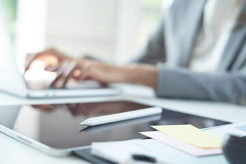 Businesswoman working on laptop computer with digital tablet and stylus pen on table at office, close up
