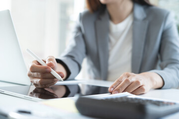 Businesswoman working at office using digital tablet and laptop computer, close up. Young female manager using stylus pen signing on tablet screen and surfing the internet on laptop at workplace