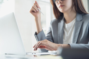 Young smart business woman working at office using laptop computer and digital tablet, close up. Asian businesswoman  planning new business project, using laptop surfing the internet, close up