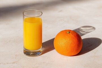 Fresh Orange Juice in Clear Glass Beside Whole Orange on Light Marble Surface