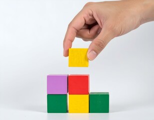 Hand placing colorful wooden block on a stack of blocks.  Concept of building, growth, strategy, planning.