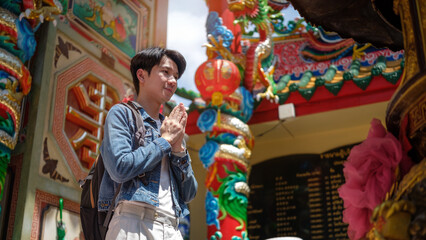 Traveler in denim jacket making a respectful wai gesture at a vibrant Chinese temple