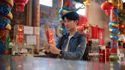 Young male traveler holding incense sticks while making a wish inside a Chinese temple